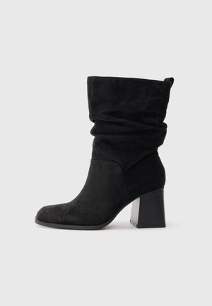 Stivaletti alla caviglia in suede nero con un design morbido, punta quadrata e tacco spesso. Presentano sottili motivi impressi sul materiale.
