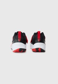 Une paire de baskets noires et rouges vues de l'arrière, avec des semelles intermédiaires blanches et des languettes rouges arborant un logo de filet de basketball.
