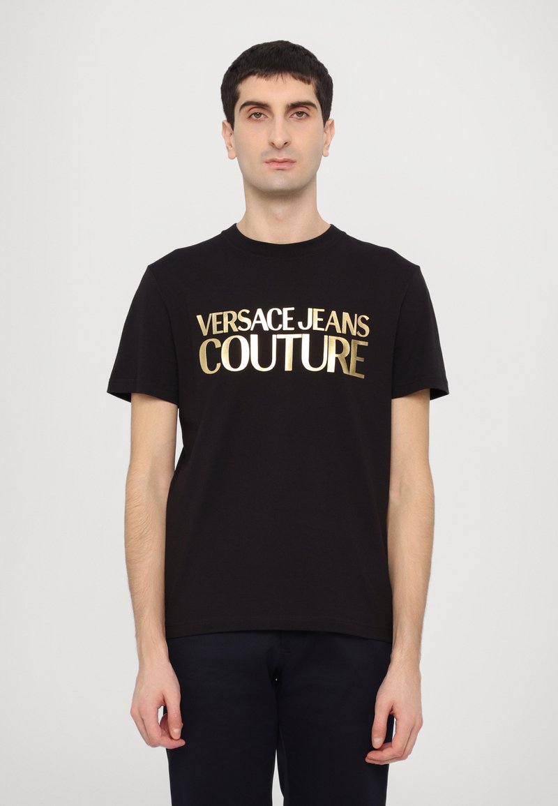 Juodas medvilnės marškinėliai trumpomis rankovėmis, su ryškiu auksiniu užrašų "VERSACE JEANS COUTURE" priekyje. Paprastas, klasikinio kirpimo dizainas.