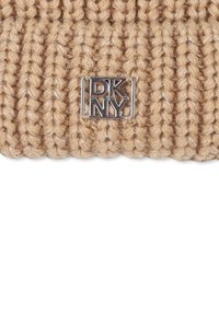 Tissu tricoté beige avec un petit logo en métal argenté où les lettres D, K, N, Y sont disposées dans un motif carré.