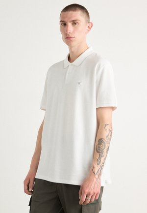 Witte polo-shirt met een kraag, korte mouwen en een subtiel logo op de borst. De stof lijkt glad, met een rechte snit.