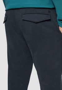 Dunkelblaue Hose mit einer glatten Textur, zwei flachen Gesäßtaschen und einem dezenten Logodetail in der Nähe des Bundes.