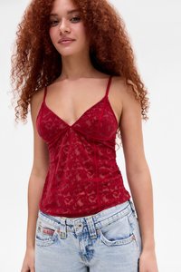 Camisola rossa in pizzo con spalline regolabili, motivo floreale e silhouette aderente, indossata con jeans blu chiaro strappati.