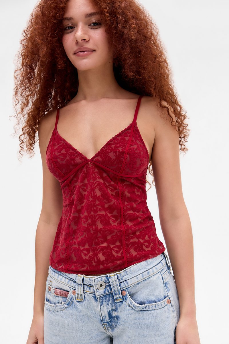 Camisola rossa in pizzo con spalline regolabili, motivo floreale e silhouette aderente, indossata con jeans blu chiaro strappati.