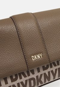 Brun clutch i tekstureret læder med DKNY-logo. Har en glat topflade og mønstret stof med store bogstaver i bunden.