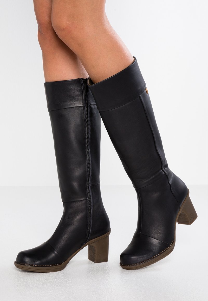 Black leather knee-high boots with a rounded toe, block heel, and side zipper. Features a smooth texture and contrasting stitching detail.