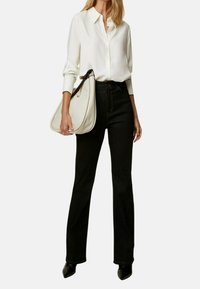 Camicia bianca con maniche lunghe, jeans flared neri a vita alta e borsa bianca, abbinati a scarpe con tacco a punta nere.
