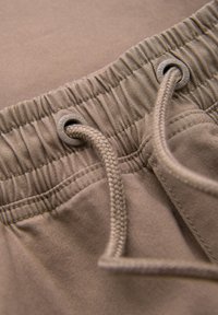 Gros plan d'une ceinture élastique beige avec un cordon tressé passant à travers des œillets métalliques sur un short ou un pantalon en tissu.