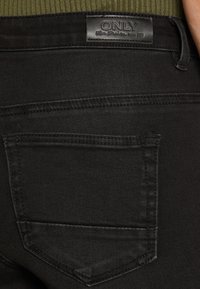Jeans de mezclilla negra con una textura distintiva, que cuentan con un solo bolsillo trasero y una etiqueta embosada "ONLY" en la cintura.