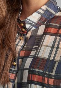 Plaid shirt with a high collar, featuring blue, white, red, and orange patterns. Gold button accents visible along the neckline.