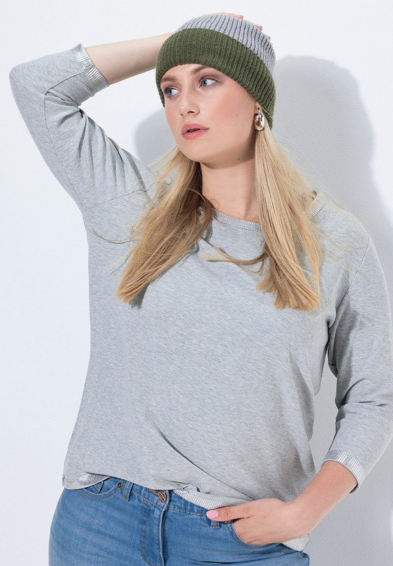 Camisa gris de manga larga con textura acanalada y detalles plateados en las mangas, combinada con un gorro de punto a rayas en verde y gris.