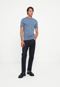 Light blue short-sleeve t-shirt in cotton with a round neckline, paired with dark denim straight-leg trousers and black loafers.