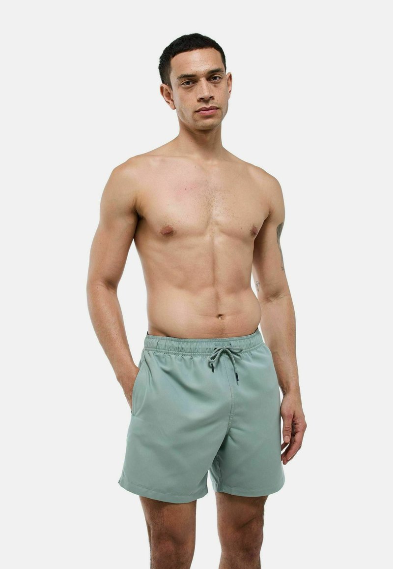 Shorts de bain vert clair en matériau lisse et à séchage rapide. Équipés d'une taille élastique, d'un cordon de serrage et de poches latérales.