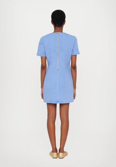 Denim dress in light blue, short sleeves, fitted design, features a visible back zipper, and a straight hem. Worn with gold slip-on shoes.