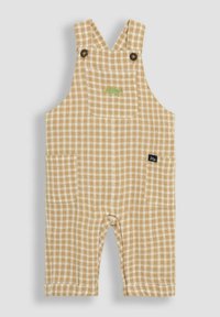 Beige overall med rutigt mönster, justerbara axelremmar, två framfickor och grön dinosauriebroderi på fickan.