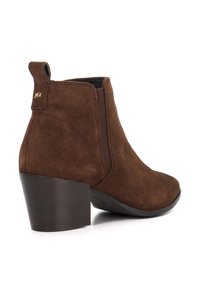 Brown suede ankle boot with a tapered heel, elastic side panels, and a pull tab at the back. Textured surface with stitched detailing.