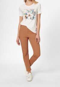 Pantalones ajustados color beige combinados con una camiseta gráfica blanca que presenta un diseño y patrones florales coloridos. Los zapatos son zapatillas blancas.