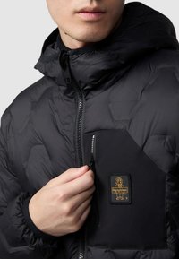 Giubbotto trapuntato nero con texture a esagoni, colletto alto, chiusura con zip e tasca sul petto con patch del logo dorato.