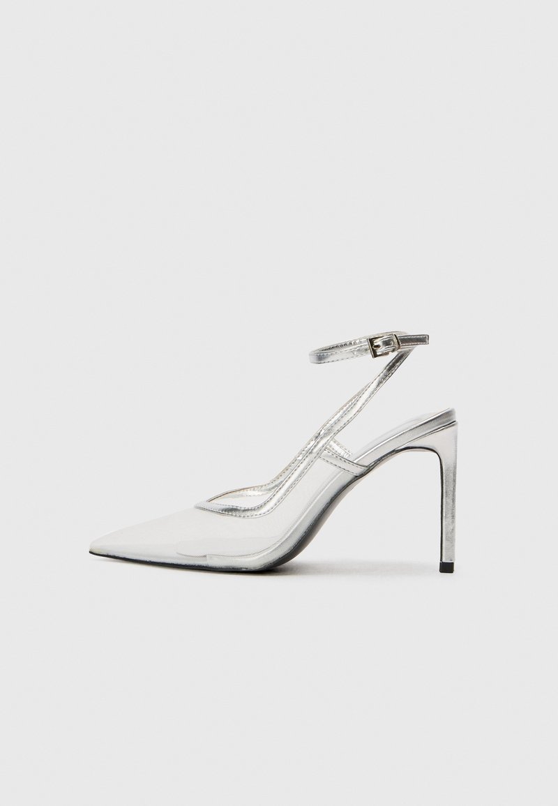 Chaussure à talon aiguille transparent avec un bout pointu, accents métalliques argentés et une bride de cheville, présentant un design épuré et une texture lisse.