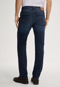 Dunkelblaue Jeans aus Denim mit geradem Bein, kontrastierenden orangen Nähten und zwei Gesäßtaschen. Ein braunes Lederlogo-Patch ist am Bund zu sehen.