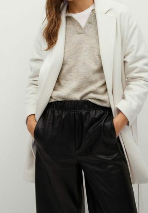 Hvid lang jakke over en lys beige sweater og sorte læderbukser med høj talje. Outfittet har en afslappet pasform og sidelommer.