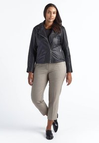 Sort lædermotorcykeljakke med lynlås foran, kombineret med beige ternede bukser. Modellen bærer sorte loafers.