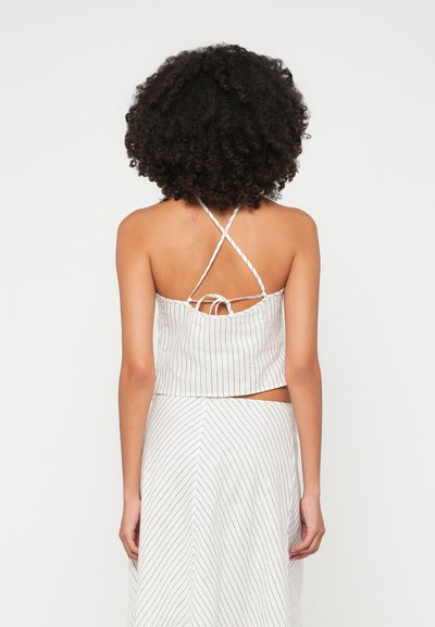 Top corto de tela ligera con finas rayas verticales, que presenta una espalda cruzada con lazos, y se complementa con una falda a juego de rayas diagonales.