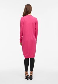 Lange roze trui met een ronde hals, geribde manchetten en zoom, met een gladde textuur en rechte lijn. Draagt over zwarte leggings.