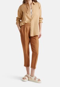 Ljuslila linne skjorta med knappar, avslappnad passform; bruna tapered byxor med upprullade fållar; krämfärgade sandaler med remmar och texturerad sula.