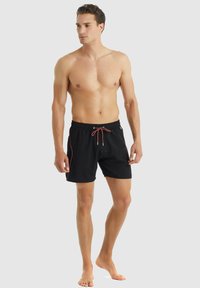 Pantaloni da mare neri con cintura elastica, cordoncino arancione e tasche laterali. Tessuto liscio con dettagli di cucitura in contrasto.