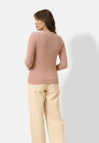 Suéter de punto de canalé en rosa claro con mangas largas y un diseño ajustado, combinado con pantalones de pierna ancha color crema, visto desde atrás.