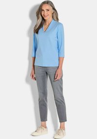 Hellblaues V-Ausschnitt-Oberteil mit drei Viertelärmeln, kombiniert mit grauen, schmal geschnittenen Hosen und beigen Sneakers; glatter Stoff und lockerer Sitz.