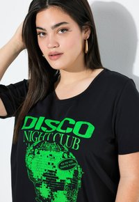 Black t-shirt featuring green graphic print of a disco ball and text "DISCO NIGHT CLUB." Short sleeves, round neckline, soft texture.