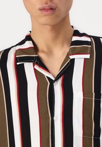 Lyhythihainen nappipaita, jossa on pystysuorat raidat mustassa, valkoisessa, punaisessa, oliivinvihreässä ja beigessä; sisältää taskun ja pehmeän kankaan tekstuurin.