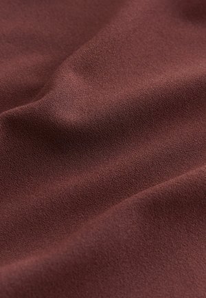 Lähikuva pehmeästä, tekstuurillisesta ruskeasta kankaasta, jossa on hienovaraisia taitoksia ja hieman karheapintainen pinta.