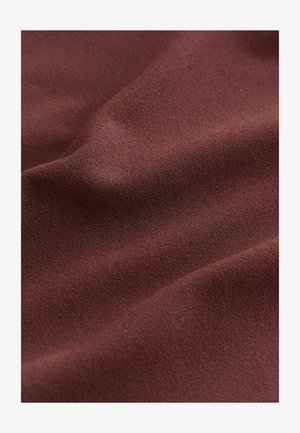 Lähikuva pehmeästä, tekstuurillisesta ruskeasta kankaasta, jossa on hienovaraisia taitoksia ja hieman karheapintainen pinta.