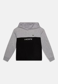 Grauer und schwarzer Hoodie mit Kängurutasche, mit einem großen weißen "LACOSTE"-Logo und einem grünen Krokodil-Emblem auf der Brust.
