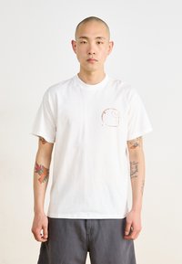 White short-sleeve t-shirt featuring a subtle graphic on the left chest area, with a relaxed fit and soft cotton texture.
