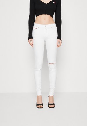 Pantalones vaqueros blancos ajustados con una rodilla desgastada, combinados con un top corto de manga larga negro con canalé. Cuenta con un cierre frontal de botón y un diseño ceñido.