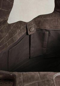 Sisemine tumepruun seemisnahast käekott, millel on trukiga kinnitus ja väike sisemine kangast tasku on nähtav.