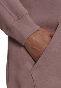 Długi rękaw z kapturem w przygaszonym mauve; posiada ściągacz przy mankietach i kieszeń z przodu, o gładkiej fakturze materiału.