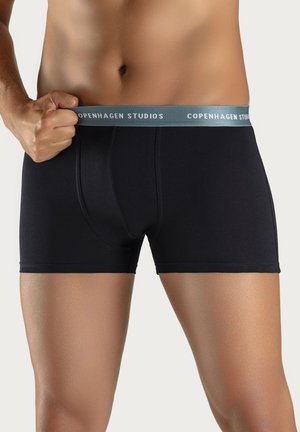 Schwarze Boxershorts mit einem hellblauen elastischen Bund, der mit "COPENHAGEN STUDIOS" beschriftet ist. Glatte Textur, enganliegendes Design und kurze Länge.