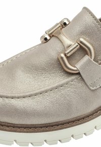 Metaalachtige beige instapschoen met een getextureerde leren bovenzijde, voorzien van een opvallende gouden gesp en een witte rubberen zool.