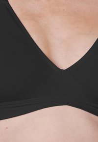 Czarny stanik z dekoltem w kształcie litery V, wykonany z gładkiego, teksturowanego materiału, z bezszwowym wykończeniem i minimalną ilością ozdób.