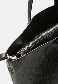 Black leather handbag with textured surface, showing an interior zip pocket and silver zipper, featuring dual handles and minimalist design.