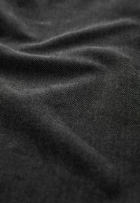 Tissu noir avec une texture lisse, présentant de subtils motifs de tissage diagonal et un drapé doux, illuminé par une lumière douce.