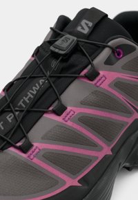 Gray athletic shoe featuring a textured upper with pink accents and a specialized lacing system for a secure fit. Smooth rubber sole.