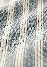 Tissu rayé bleu et blanc. La texture est douce avec un motif tissé frappant, comportant des rayures alternées fines et épaisses.