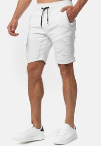 Pantalones cortos blancos con un diseño texturizado, que presenta acentos ribeteados horizontales, detalles desgastados, cinturilla elástica y cordón negro.