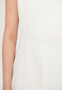 Λευκό αμάνικο φόρεμα με ομαλή υφή, εφαρμοστό μπούστο και φαρδιά λουρίδα στο τελείωμα. Ορατή ραφή κατά μήκος των πλαϊνών ραφών.